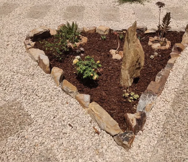 Planted garden bed outlined with natural stones, bark mulch and an upright feature stone