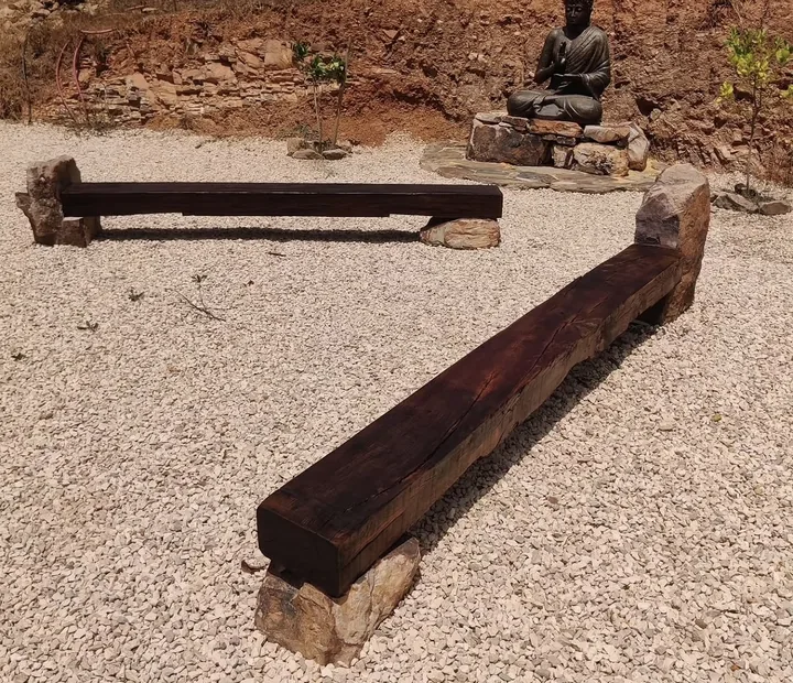 Two dark timber garden benches resting on natural stone supports in a gravel seating area